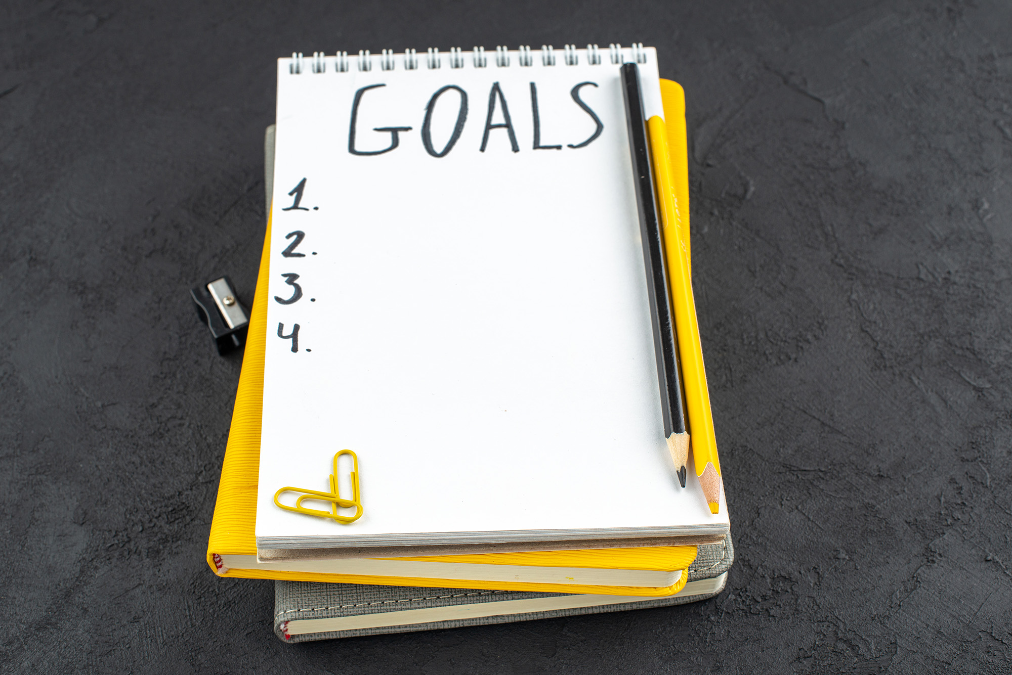 bottom view list goals written notepad pencil sharpener black yellow pencils gems clips dark background web
